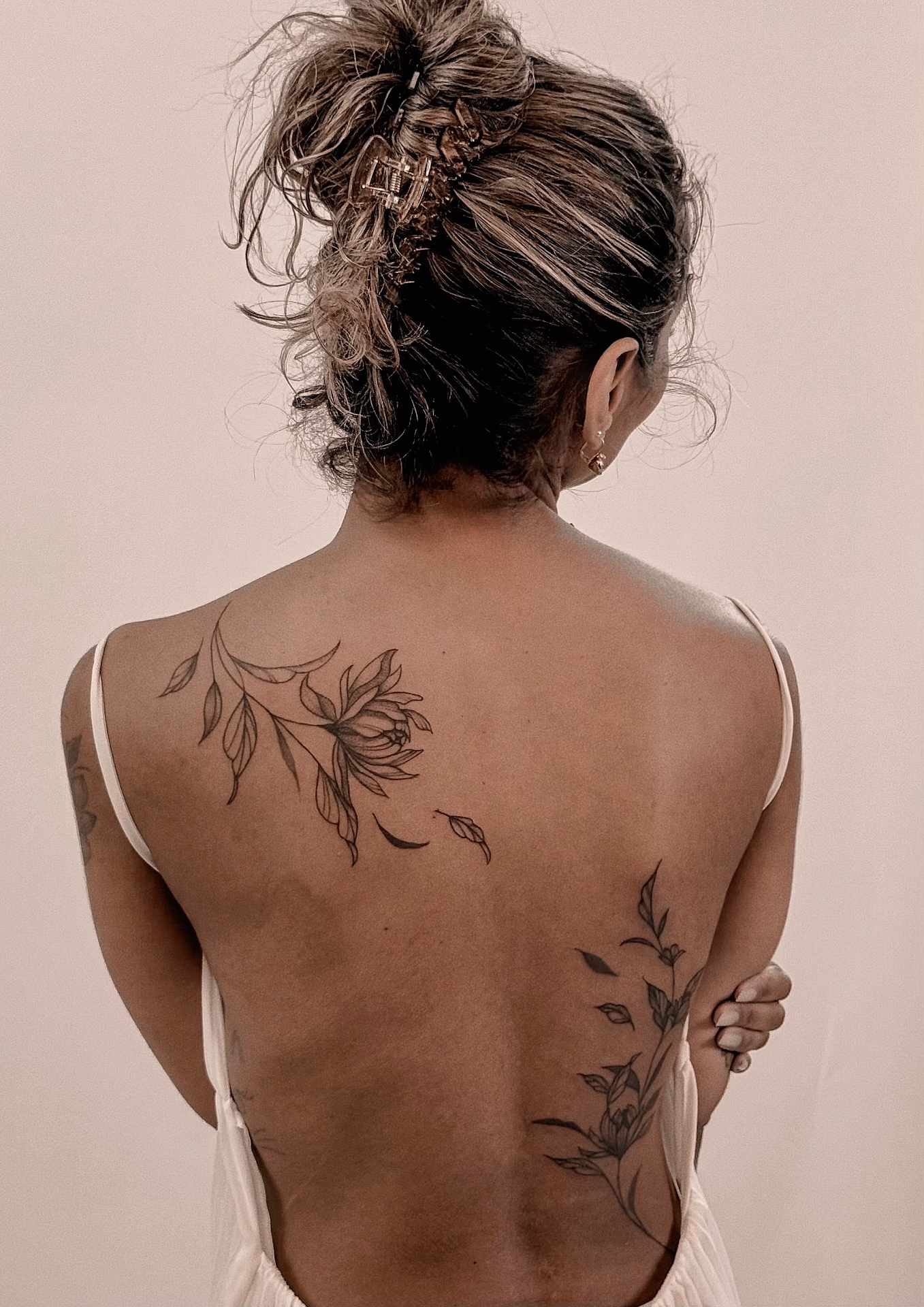 Two fine line floral sprigs with drifting petals tattooed on the back